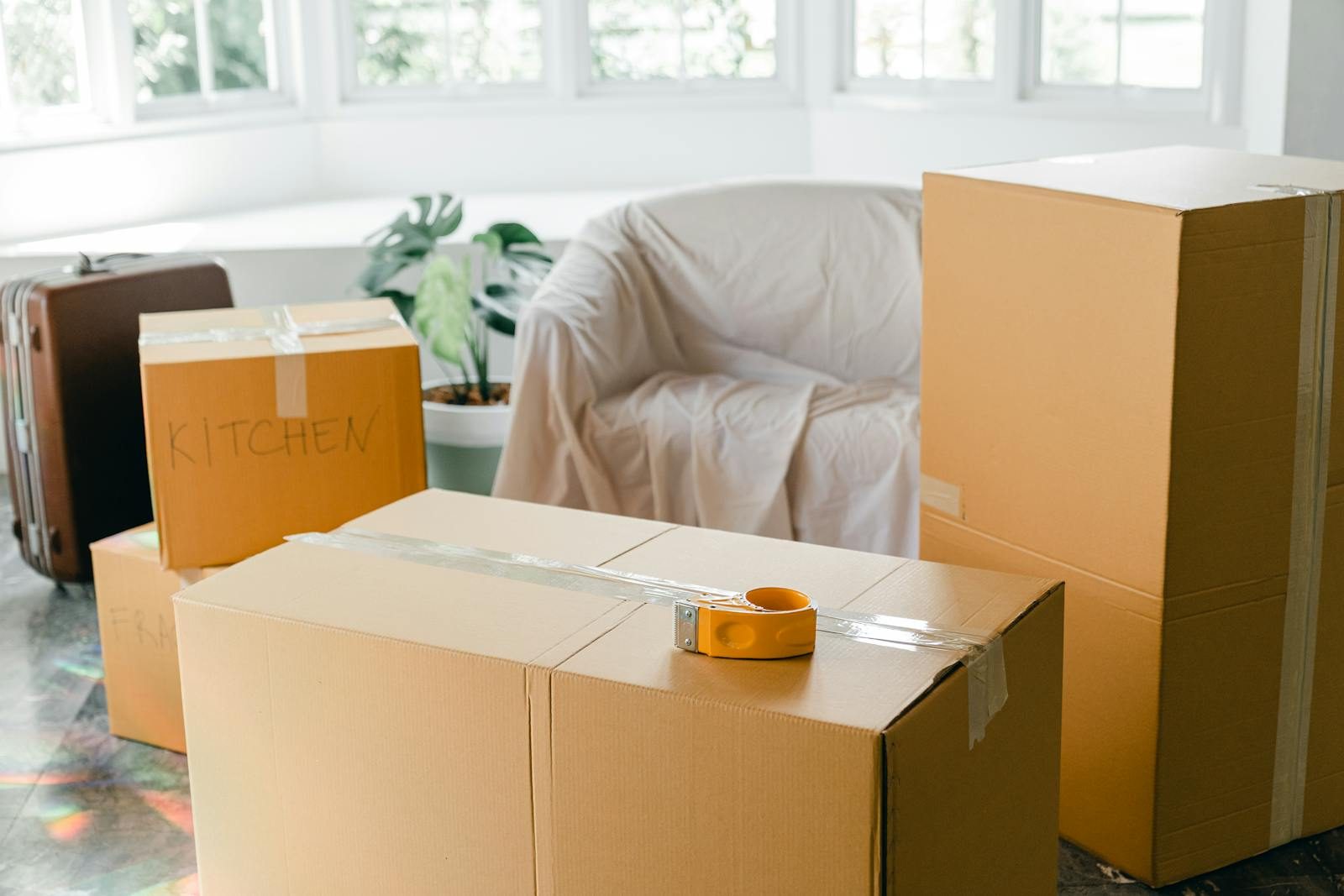 Packed moving boxes with a tape gun on top in an empty Sydney room ready for the removalist